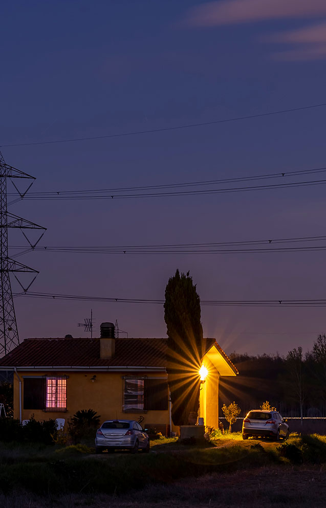 vista notturna di una casa con luci accese e un traliccio dell'energia elettrica sullo sfondo